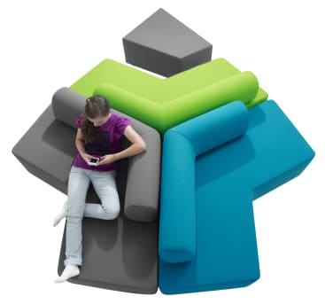 Eine Person sitzt auf einem modularen, sternförmigen Sofa mit grauen, grünen und blauen Teilen und zylindrischen Rückenlehnen und schaut auf ein Smartphone. Das Sofa steht vor einem weißen Hintergrund.