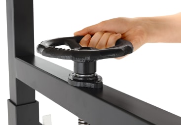 Die Hand einer Person dreht ein großes schwarzes Metallrad, das an einer Maschine befestigt ist, vor einem weißen Hintergrund.