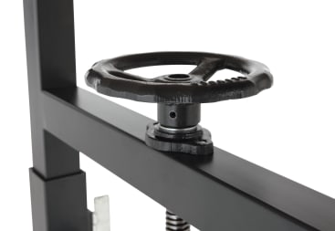 Nahaufnahme eines schwarzen Metallhandrads, das an einem rechteckigen Metallrahmen befestigt ist, wahrscheinlich Teil einer Industriemaschine oder mechanischen Presse, vor einem weißen Hintergrund.