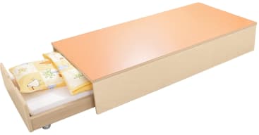 Ein helles Holzausziehbett mit orangefarbenem Bezug. Das untere Bett ist teilweise ausgezogen und zeigt Bettzeug mit gelben und weißen Laken und ein Kissen mit bunten Mustern. Das Bett hat Räder für eine einfache Bewegung.
