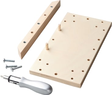 Eine Holzschablone mit mehreren Löchern, zwei Holzdübel, ein L-förmiges Holzstück mit Metalleinsätzen, drei Schrauben und ein Schraubendrehergriff mit Metallschaft, alles auf weißem Hintergrund.