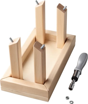 Ein kleiner rechteckiger Holztisch, der auf den Kopf gestellt ist und dessen vier Beine mit Schrauben, einem Schraubenzieher, einer Unterlegscheibe und einer Mutter befestigt sind, steht in der Nähe auf einem weißen Hintergrund.
