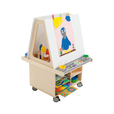 Eine hölzerne Kinderstaffelei auf Rädern, unter der Farbflaschen und Zubehör aufbewahrt werden, ein Tablett mit Farbbechern und Pinseln und ein buntes Gemälde eines blauen Vogels, das an der vorderen Anzeigetafel befestigt ist.