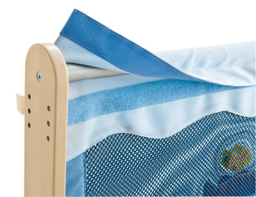Nahaufnahme der Ecke eines Kinderbettgitters, die einen Holzpfosten, hellblauen Stoff, ein blaues Mesh-Paneel und ein blaues Klettband zeigt, mit dem der Stoff am Pfosten befestigt ist.