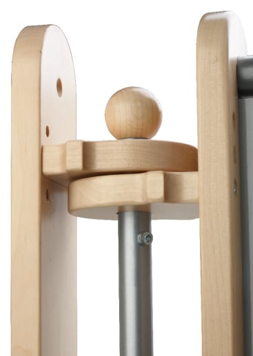 Nahaufnahme einer Holzstruktur mit abgerundeten Kanten und einer runden Holzkugel, die auf einer kleinen Plattform ruht und an einer vertikalen Metallstange mit einer Schraube befestigt ist.
