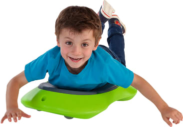Ein kleiner Junge in blauem Hemd und Jeans liegt auf dem Bauch auf einem hellgrünen Spielzeug auf Rädern und lächelt in die Kamera, während er die Arme nach vorne streckt und einen Fuß hinter sich hebt.
