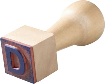 Ein hölzerner Stempel mit einem Griff, der einen erhabenen blauen Buchstaben D auf einem quadratischen Sockel zeigt, der an den Seiten leicht mit blauer Tinte befleckt ist.