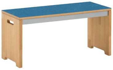 Eine Holzbank mit einer blauen rechteckigen Sitzfläche, hellen Holzbeinen und ausgeschnittenen Griffen an den Seiten. Die Bank hat ein einfaches, modernes Design und ein robustes Aussehen.