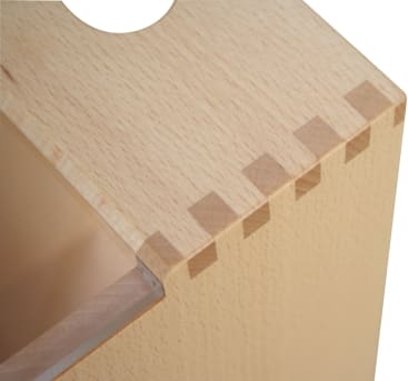 Nahaufnahme einer hölzernen Kastenecke, die die Schwalbenschwanzverbindungen zwischen den Seiten zeigt; das Holz ist hell und glatt und hat eine kreisförmige Aussparung auf der oberen Platte.