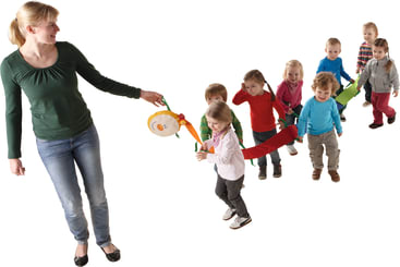 Eine erwachsene Frau führt eine Gruppe junger Kinder, die sich an einem bunten Seil festhalten, in einer Reihe an. Die Kinder sind leger gekleidet und scheinen alle vorwärts zu gehen. Der Hintergrund ist weiß.