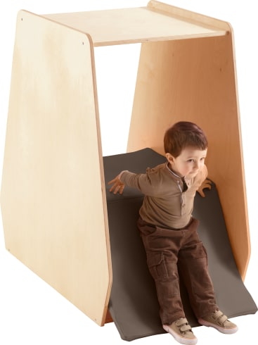 Ein Kleinkind rutscht eine gepolsterte Rampe hinunter, die an einem kleinen Holzspielgerät befestigt ist. Das Kind stützt sich mit den Händen ab, während es die Rampe hinunterrutscht.