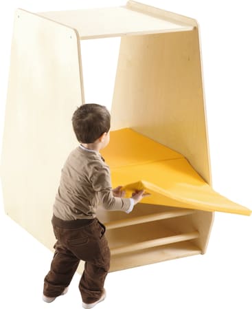 Ein kleines Kind legt eine gelbe Matte auf das untere Regal eines hellen Holzschranks mit offenen Seiten und zwei Regalen.