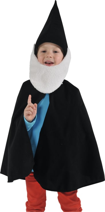 Ein Kind mit einer schwarzen Zipfelmütze, einem langen weißen Bart, einem schwarzen Umhang, einem blauen Hemd und einer roten Hose, das als Gnom verkleidet ist, steht da und lächelt mit erhobenem Finger.