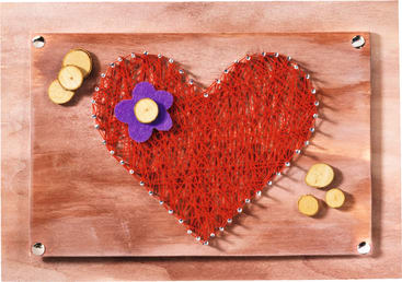 Ein Holzbrett mit einer roten String-Art-Herzform, verziert mit einer kleinen lila Filzblume und mehreren runden Holzteilen, die durch silberne Nägel an den Rändern des Herzens zusammengehalten werden.