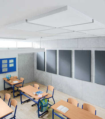 Ein modernes Klassenzimmer mit Holzschreibtischen, blauen Stühlen, einem grünen Rucksack, Büchern und einem Globus. An den Wänden und der Decke sind graue Akustikplatten angebracht. An der linken Wand befindet sich eine blaue Pinnwand. Der Raum ist menschenleer.