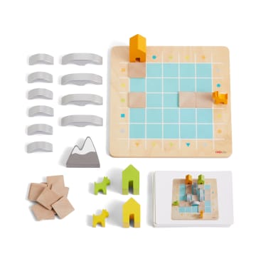 Ein Brettspiel aus Holz mit einem Gitterbrett, grauen Bögen, Holzblöcken, einem Berg, grünen und gelben Tier- und Hausplättchen und illustrierten Karten, die alle ordentlich auf einem weißen Hintergrund angeordnet sind.