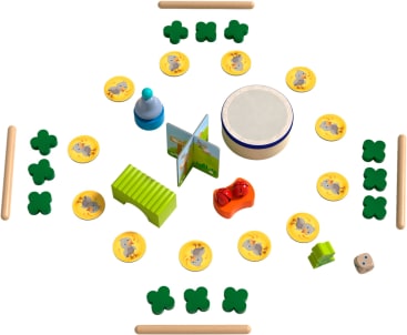 Eine Vielzahl von Kinderspielzeug und Spielfiguren, darunter hölzerne Kleeblätter, Tierplättchen, eine Trommel, ein Buch, eine Glocke, eine rote Rassel, ein Xylophon, Würfel und Holzstäbchen, die in einem symmetrischen Muster angeordnet sind.
