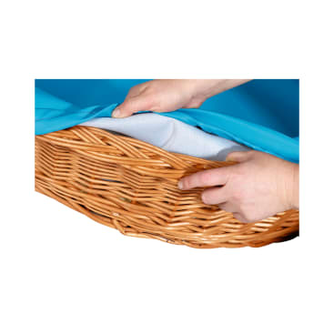 Eine Nahaufnahme von zwei Händen, die ein blaues Laken oder einen Stoff über ein weißes Futter in einem geflochtenen Weidenkorb stülpen.