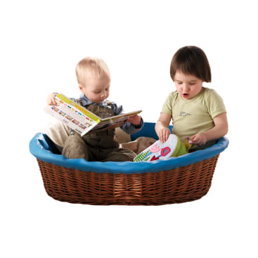 Zwei kleine Kinder sitzen zusammen in einem braunen Weidenkorb mit blauem Rand. Ein Kind liest ein Buch, während sich das andere ein buntes Spielzeug ansieht. Der Hintergrund ist einfarbig weiß.
