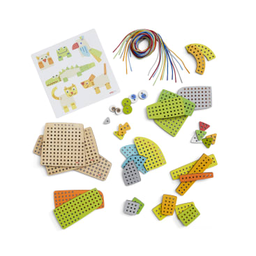 Verschiedene geometrische Holzteile mit Löchern, bunte Schnürsenkel, Plastikverbinder und eine Karte mit Tiermotiven sind auf einer weißen Fläche angeordnet. Die Teile sind verteilt und nach Typen geordnet.