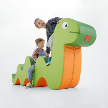 Zwei Kinder spielen auf einem großen, weichen, grün-orangenen, raupenförmigen Gebilde. Ein Kind lächelt, während es oben auf dem Kopf sitzt, das andere sitzt weiter hinten und schaut nach unten. Der Hintergrund ist einfarbig weiß.