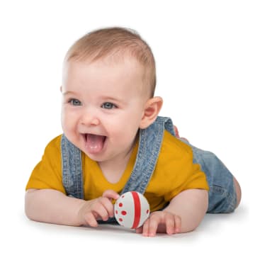 Ein Baby in einem gelben Hemd und einem Jeans-Overall liegt auf dem Bauch, lächelt mit offenem Mund und hält einen kleinen Ball mit roten und weißen Streifen vor einem weißen Hintergrund.