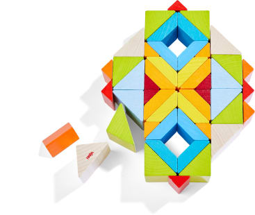Mehrere bunte Holzklötze sind in einem symmetrischen Muster angeordnet, wobei zwei lose Klötze - ein orangefarbenes rechteckiges und ein weißes dreieckiges Stück - nebeneinander auf einem weißen Hintergrund platziert sind.
