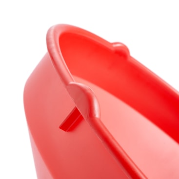 Eine Nahaufnahme des Randes und der Seite eines roten Plastikeimers vor weißem Hintergrund. Das Bild hebt einen Griffbefestigungspunkt am Rand des Eimers hervor.