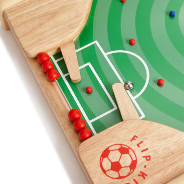 Nahaufnahme eines hölzernen Tischfußballspiels mit zwei Flossen, roten Perlen an einer Torstange und einem kleinen Metallball auf einem grünen, mit weißen Linien markierten Feld.