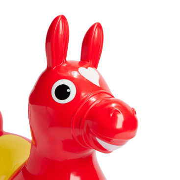Eine Nahaufnahme eines roten aufblasbaren Spielzeugpferdes mit einem weißen Herz auf der Stirn, großen schwarz-weißen Augen und aufrechten Ohren. Das Spielzeug hat außerdem einen gelben Sattel auf dem Rücken.