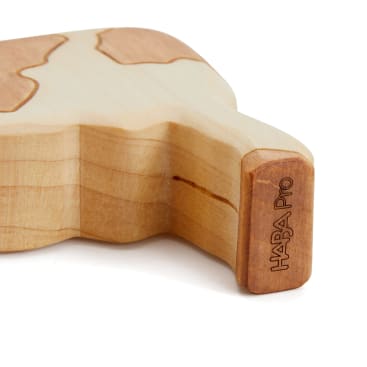 Eine Nahaufnahme eines hellen Holzspielzeugs mit geschwungenen Kanten und puzzleartigen Formen. Auf der Seite ist der Schriftzug HABA PRO eingraviert. Das Spielzeug hat eine natürliche Holzmaserung und glatte, abgerundete Konturen.