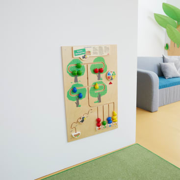 Ein hölzernes Spielbrett mit bunten, interaktiven Spielzeugen ist an einer weißen Wand in einem hellen Raum angebracht. Ein Teil einer grauen Couch mit blauen Kissen und eine grüne Spielmatte sind in der Nähe zu sehen.