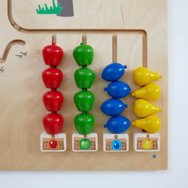Eine hölzerne Lerntafel mit vier vertikalen Stäben, die rote Äpfel, grüne Äpfel, blaue Birnen und gelbe Birnen halten. Jede Stange hat vier passende Gegenstände über einem Bild der entsprechenden Frucht in einem Korb.