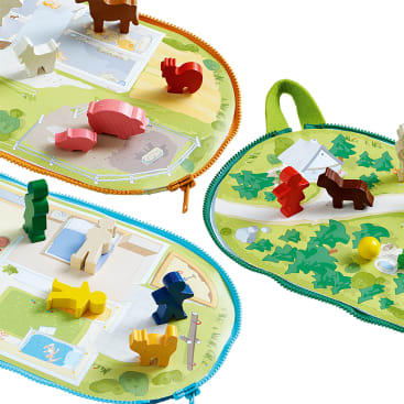 Drei farbenfrohe Spielmatten mit Reißverschluss sind geöffnet und zeigen jeweils illustrierte Hintergründe und verschiedene Tier- und Menschenfiguren aus Holz, die auf ihren Oberflächen angeordnet sind. Die Matten zeigen verschiedene Umgebungen, wie einen Park und einen Wald.