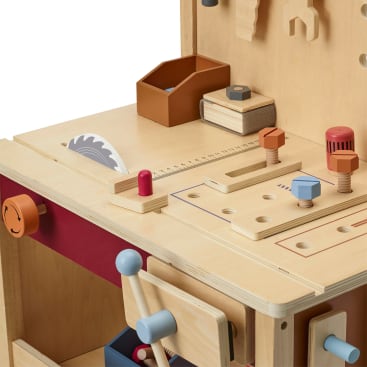 Eine hölzerne Spielzeug-Werkbank mit verschiedenen Funktionen wie einer Spielzeugsäge, Schrauben, einem Schraubenschlüssel, einer kleinen braunen Aufbewahrungsbox und Hebeln. Die Werkbank hat Löcher, Markierungen und bunte Knöpfe für interaktives Spielen.