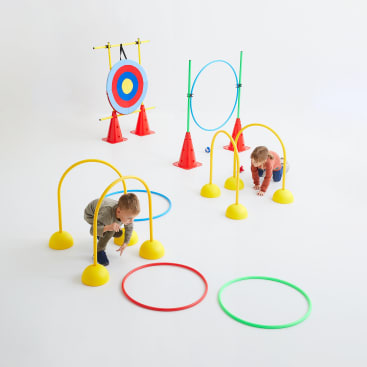 Zwei kleine Kinder krabbeln durch gelbe Bögen als Teil eines Indoor-Hindernisparcours, mit bunten Ringen auf dem Boden und einem Ziel auf Kegeln im Hintergrund, alles vor einem schlichten weißen Hintergrund.