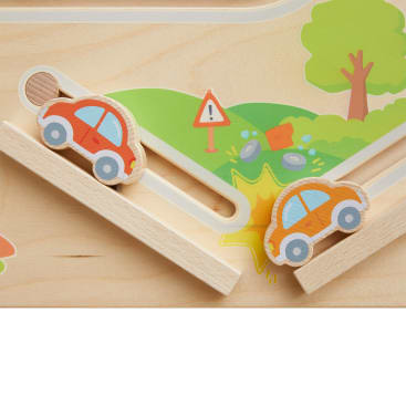 Zwei Spielzeugautos aus Holz fahren auf einer schrägen Holzbahn mit einem gemalten Hintergrund, der einen Baum, Felsen, Gras und ein Warnschild zeigt. Ein Auto befindet sich am oberen Ende der Rampe, das andere in der Nähe einer gelb gemalten Unfallstelle.