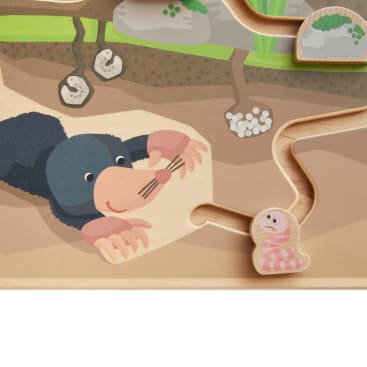 Ein Holzpuzzle zeigt einen Cartoon-Maulwurf, der unter der Erde nach einem rosa-weiß gestreiften Wurm greift; beide sind in einem spielerischen Stil mit einem labyrinthartigen Weg zwischen ihnen dargestellt.