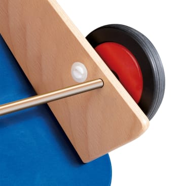 Nahaufnahme einer Holzstruktur mit einer Metallstange, einem an einem Ende angebrachten rot-schwarzen Rad und einer blauen flachen Oberfläche, die teilweise vor einem weißen Hintergrund sichtbar ist.