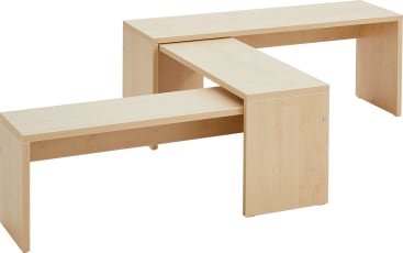 Zwei Bänke aus hellem Holz kreuzen sich in einem rechten Winkel und bilden eine L-Form mit klaren, einfachen Linien. Die Bänke haben flache Oberseiten und massive Seiten, mit sichtbaren Schrauben an den Ecken.
