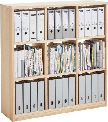 Ein Bücherregal aus hellem Holz mit acht Fächern, die jeweils eine Kombination aus weißen und grauen Aktenkisten und verschiedenen Büchern in vertikaler und horizontaler Anordnung enthalten.