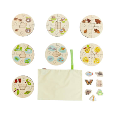 Sechs runde Holzpuzzle mit Tier- und Insektenabbildungen sind über einem cremefarbenen Stoffbeutel mit grünem Griff angeordnet. Vier Holzteile in Tierform befinden sich rechts neben dem Beutel.