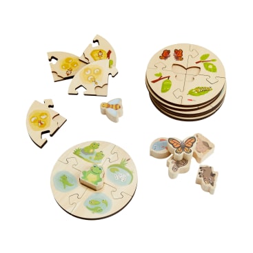 Vier runde Holzpuzzles, die den Lebenszyklus von Tieren darstellen, wobei jedes Puzzle in einzelne Teile zerlegt ist. Zusätzliche tierförmige Teile, darunter ein Frosch und ein Schmetterling, sind neben den Puzzles auf weißem Hintergrund zu sehen.