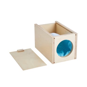 Eine rechteckige Holzkiste mit offener Oberseite und einer kreisförmigen Öffnung auf einer Seite, in der sich ein blauer Tunnel befindet. Der flache Holzdeckel wird neben die Kiste gelegt.