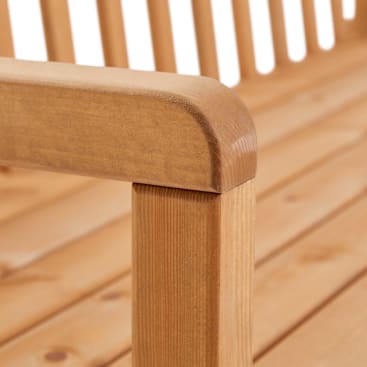 Die Nahaufnahme einer Holzbank zeigt die glatte, abgerundete Armlehne und die vertikalen Latten an Sitz und Rückenlehne. Das Holz hat eine helle, natürliche Oberfläche.