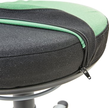 Nahaufnahme eines schwarz-grünen gepolsterten Sitzes mit einem sichtbaren Reißverschluss entlang der Kante, der teilweise geöffnet ist und die Sitzpolsterung freilegt. Der Sitz ist auf einem Metallgestell mit Rädern montiert.