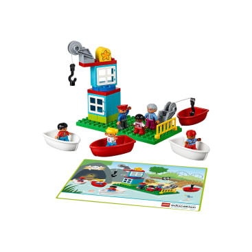 Ein LEGO Education Set mit einem bunten Kran und einem Gebäude, vier Kinderfiguren in kleinen Booten, einer Erwachsenenfigur, einem Rettungsring und einer Spielmatte mit einer Szene am Wasser.