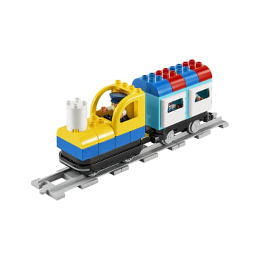Eine Spielzeugeisenbahn aus bunten, ineinander greifenden Steinen mit einer gelben Lokomotive und blau-weißen Personenwagen, die auf einem kurzen grauen Gleisabschnitt stehen. Im Führerstand der Lokomotive sitzt eine kleine Figur.