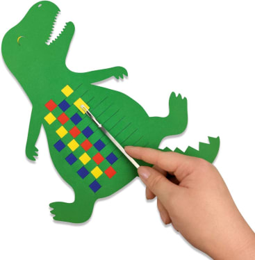 Eine Hand webt farbige Papierstreifen durch einen grünen Papierausschnitt in Form eines Dinosauriers. Die Streifen bilden ein schachbrettartiges Muster auf dem Körper des Dinosauriers.