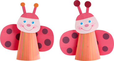 Zwei Marienkäfer aus Papier mit rosa Flügeln und roten Flecken, lächelnden Gesichtern, blauen Augen und gestreiften Kegelkörpern. Jeder hat zwei Fühler mit runden Spitzen und runde, errötende Wangen.